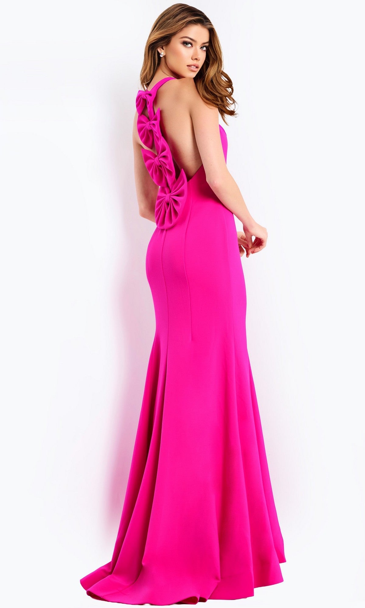 A woman stands against a plain background in the Long Prom Dress: Jovani 47639—a bright pink gown with a fitted bodice, floral open-back details, and a striking mermaid silhouette.